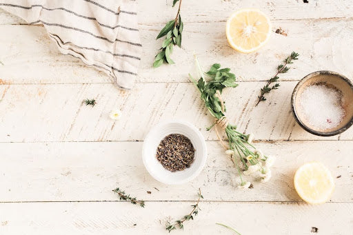 Dried herbs, plant oils, and botanical skincare bottles arranged on a pale linen surface